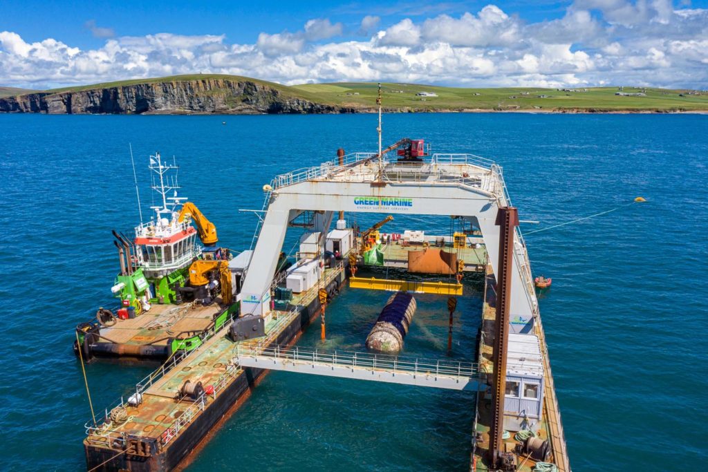 A retrieving vessel hoisting up the Northern Isles datacenter, with the Orkney Islands in the background