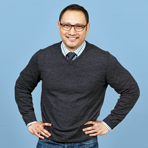 Jean Lozano stands in front of a blue background with his arms on his hips