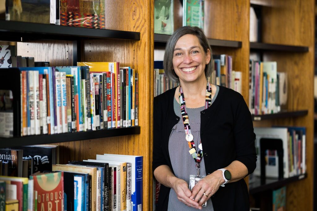 Woman smiles and leans on a bookshelf