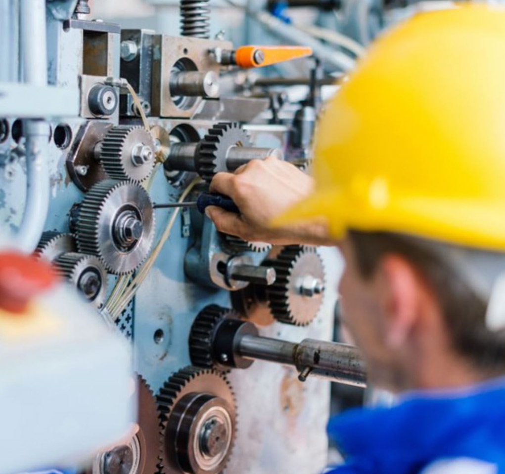 Man in a hard hat adjusts a gear in a manufacturing facility