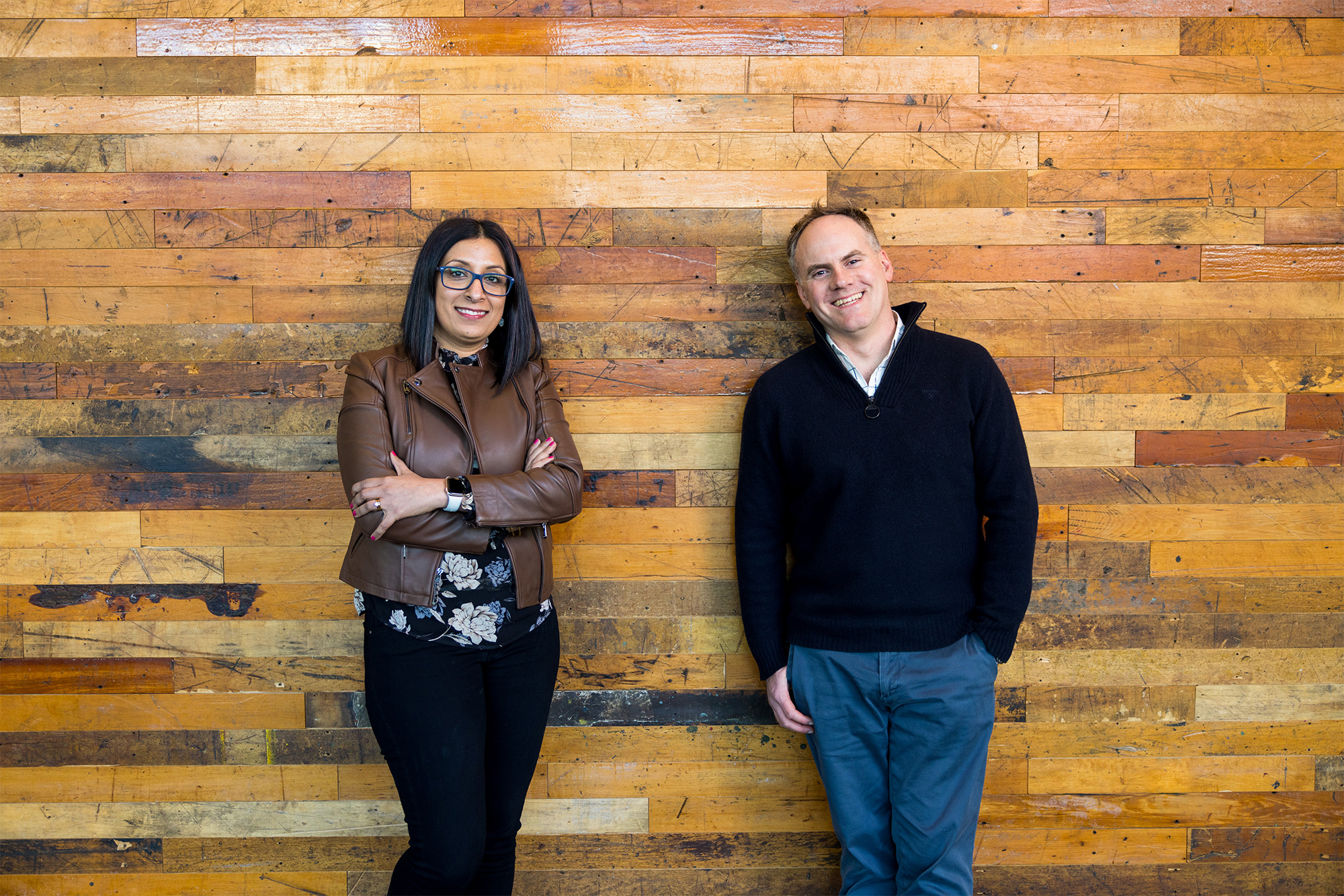 Nidhi Chappell, Microsoft head of product for Azure high performance computing, and Phil Waymouth, Microsoft principal program manager in charge of strategic partnerships. Nidhi is on the left, Phil on the right. They are standing against a wood wall.