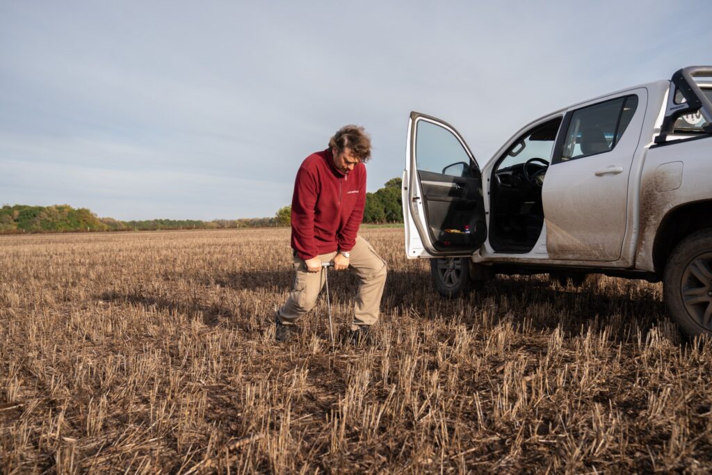 A man kneels in a field next to a truck