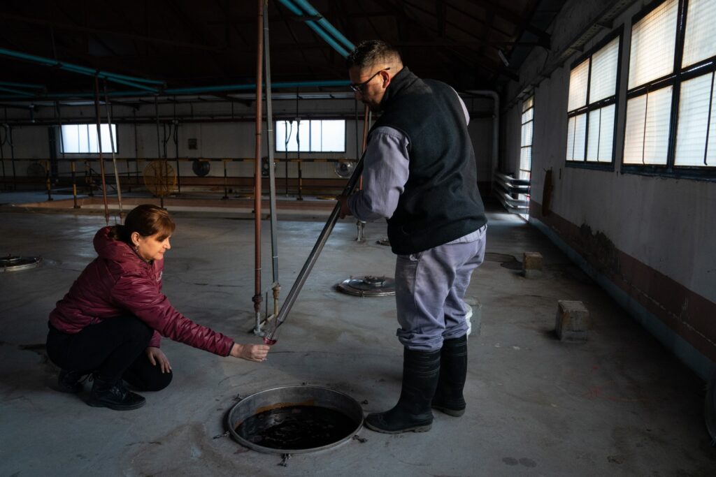 A woman kneels with a wine glass while a man stands and pours wine into it