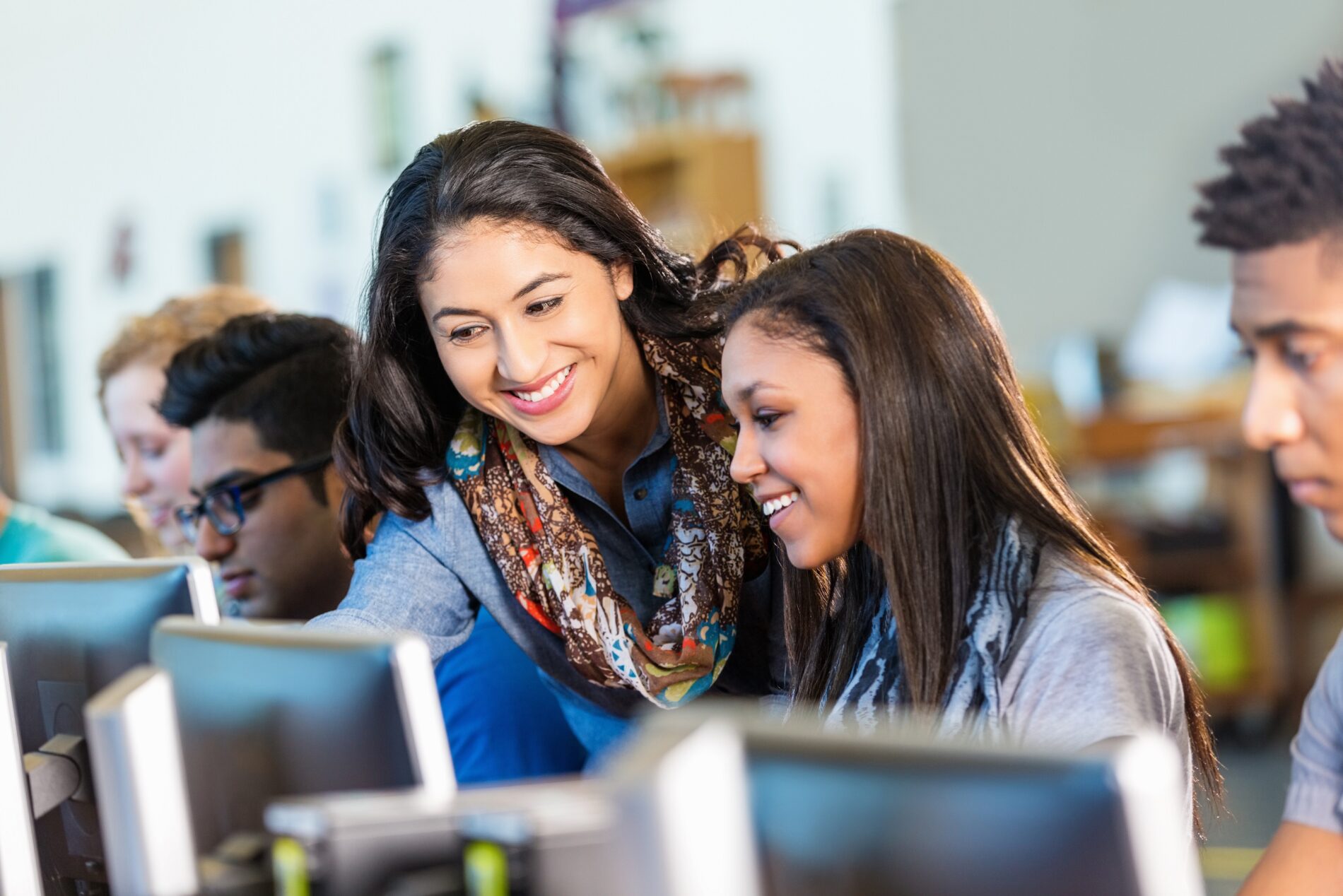 A teacher helps her students as they work on laptop computers