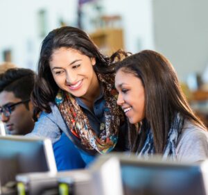 A teacher helps her students as they work on laptop computers