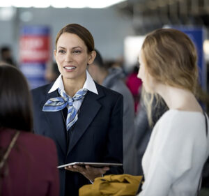 Airline stewardess holding a tablet device as she talks with two travelers