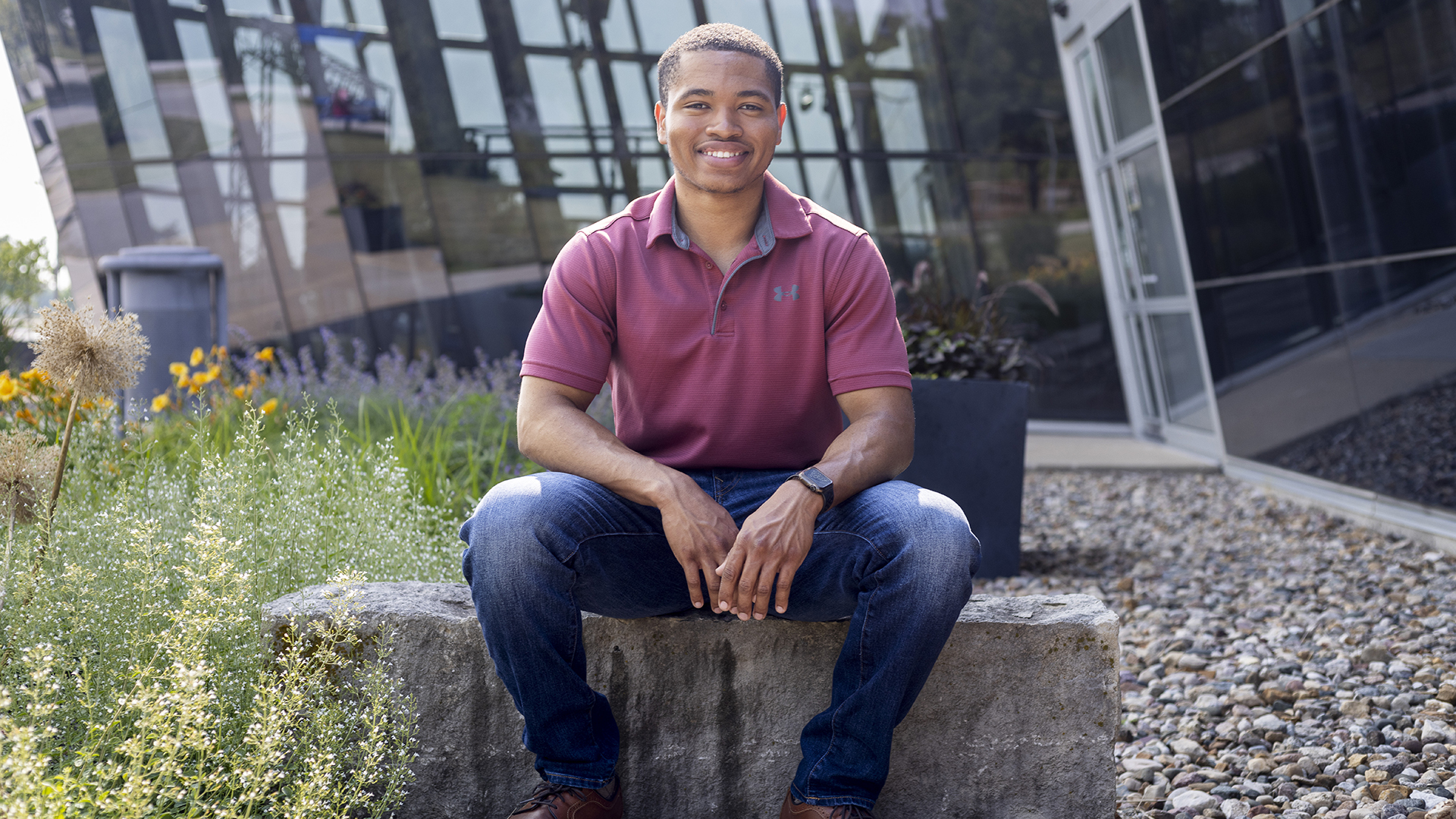 A man sits on a stone bench outside in front of a glass building