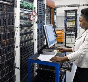 A woman works on a mobile computer station next to a server rack