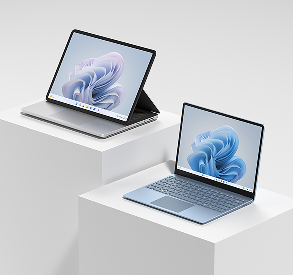 Surface Laptop Studio 2 (Platinum) and Surface Laptop Go 3 (Ice Blue) sitting on white tables