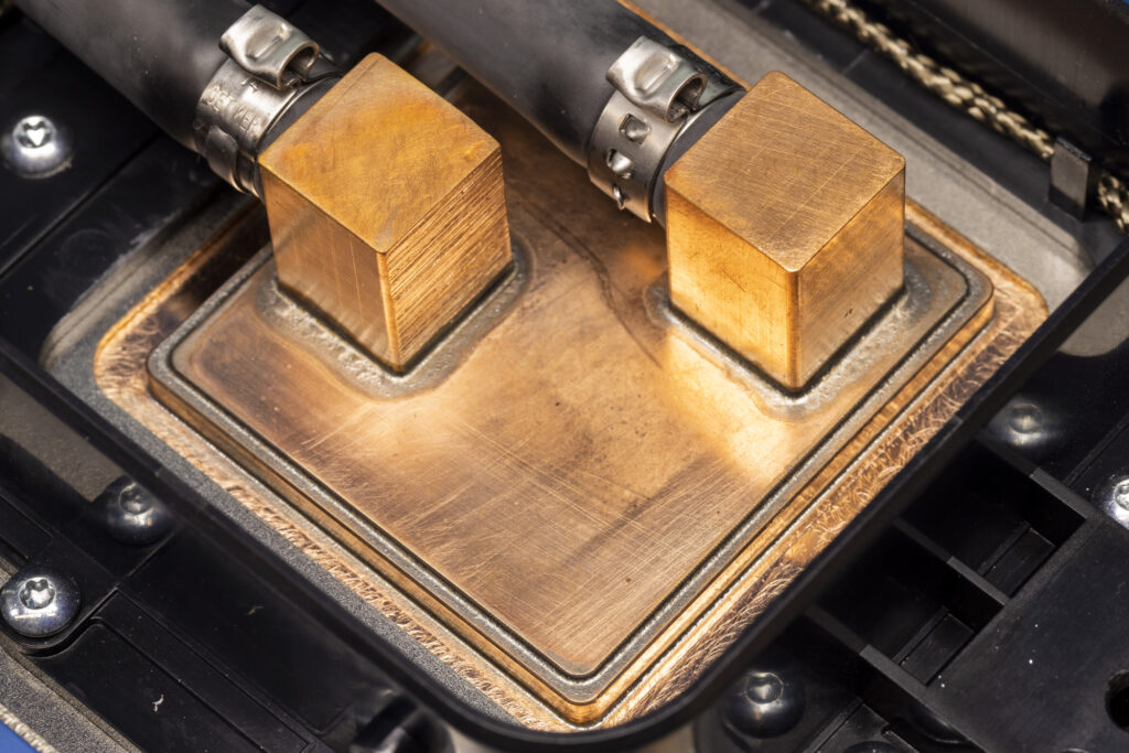 Two square blocks connect pipes to the surface of a chip that carry liquid to cool the chip.