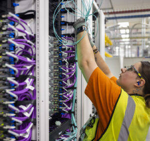 A man and a woman work to install a row of servers with colorful wires and lights.