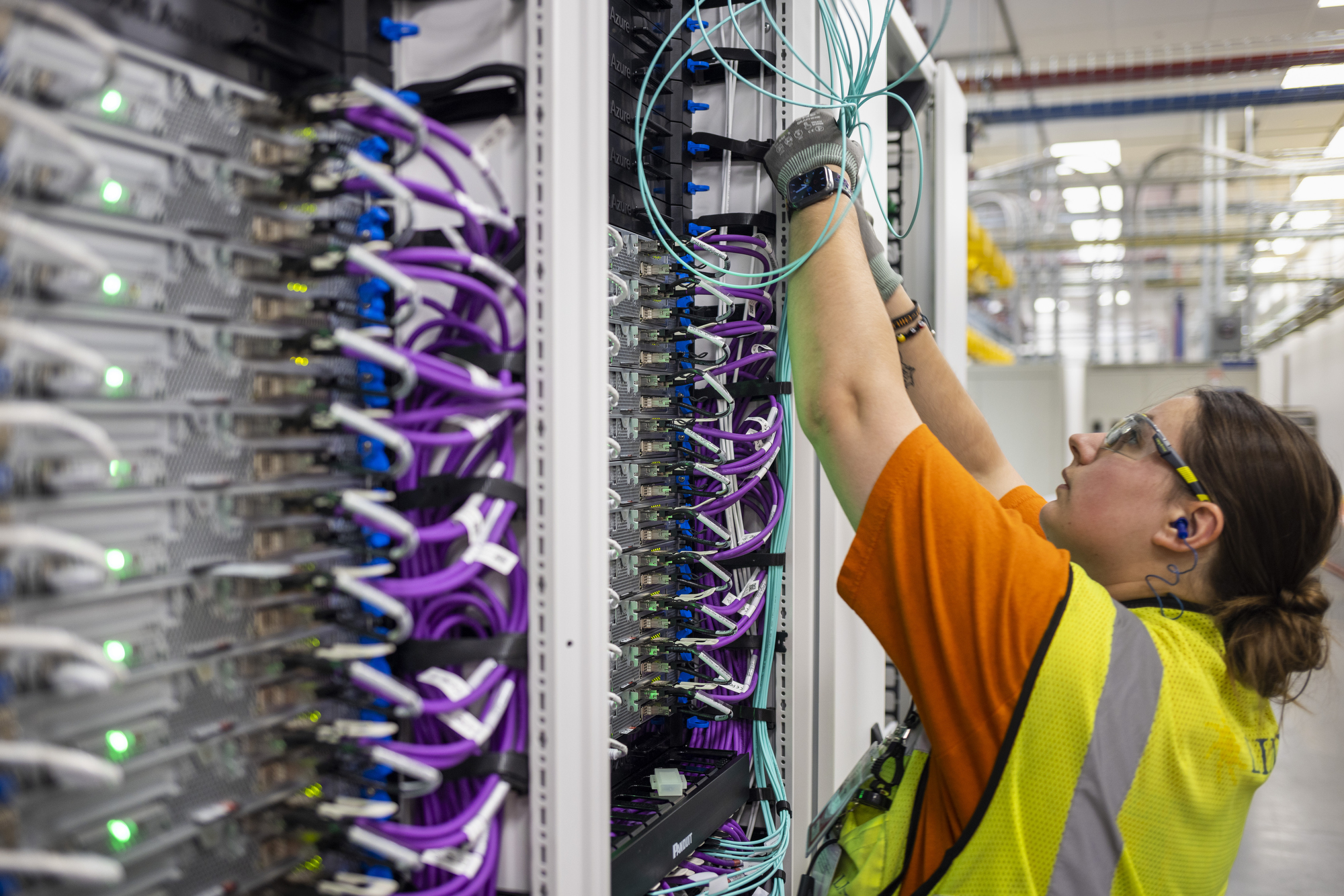 A man and a woman work to install a row of servers with colorful wires and lights.