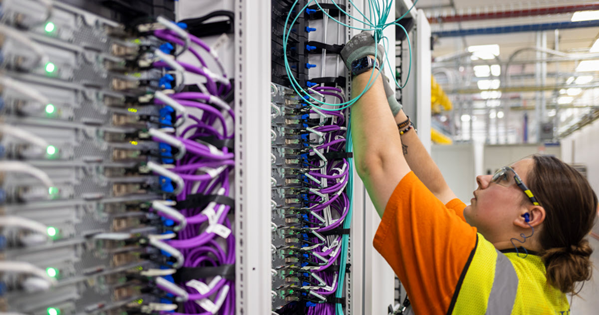 A man and a woman work to install a row of servers with colorful wires and lights.