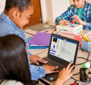 Two girls share a laptop computer in a classroom