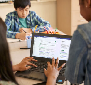 View from behind a student's head as she types onto a laptop computer along with two other students