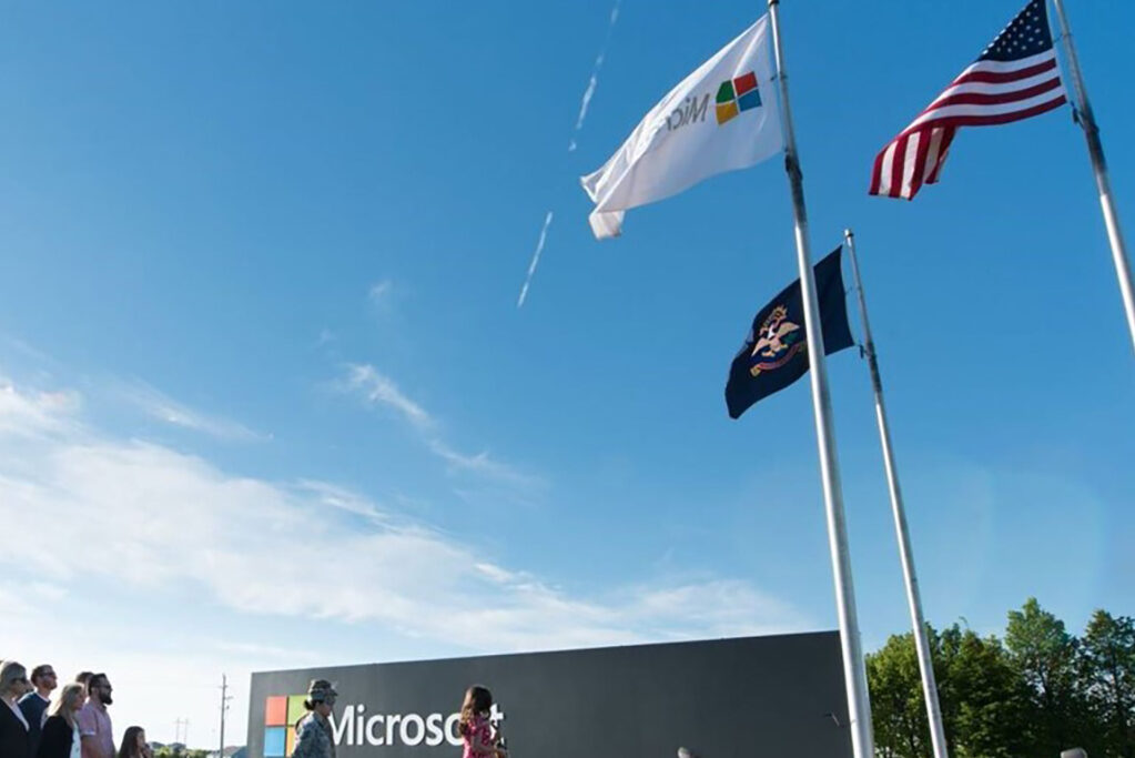 A group of people gathers below flags flying above the Microsoft campus