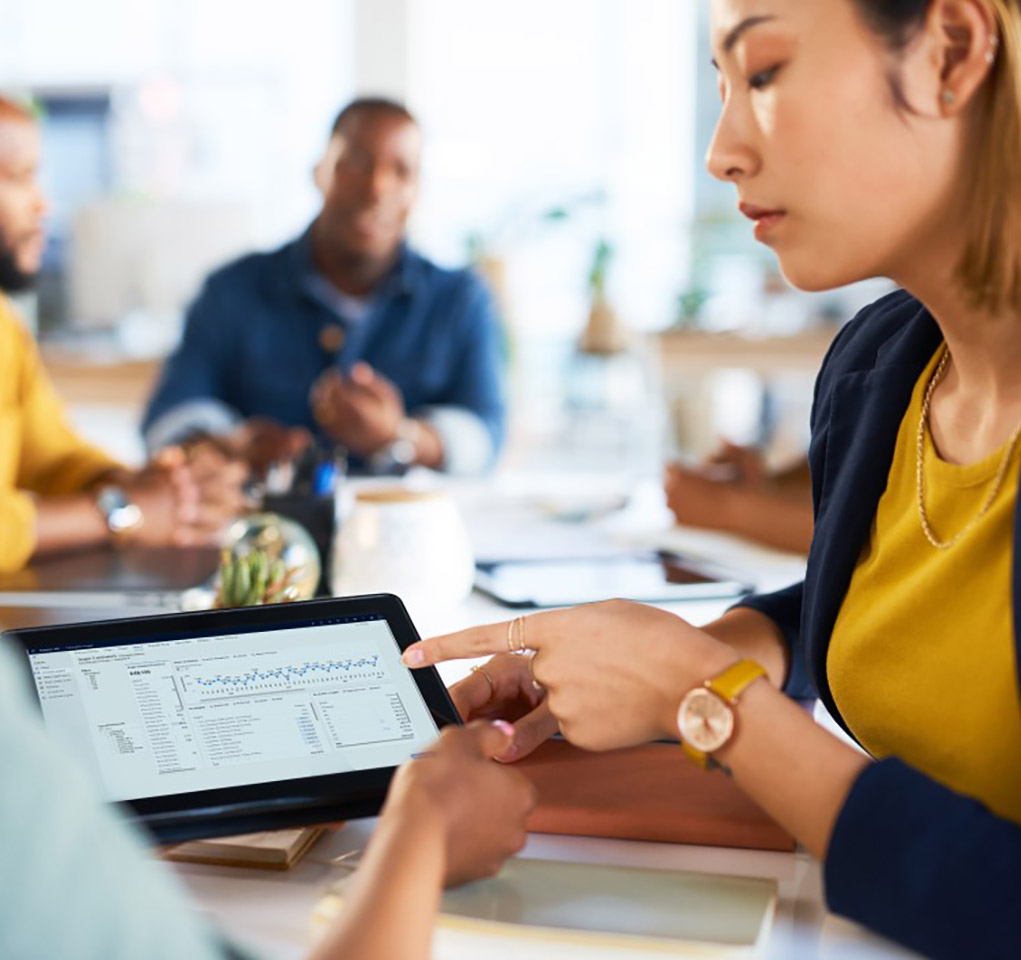 Woman in a meeting points to data displayed on a tablet device