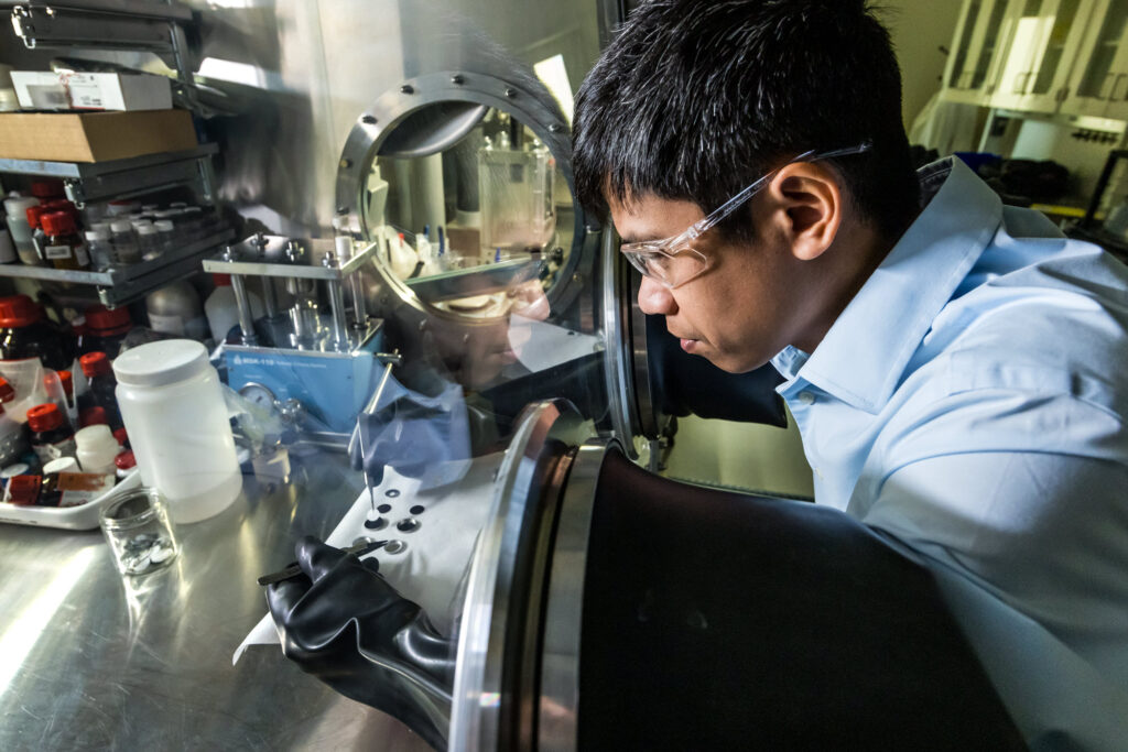 A male scientist assembles a coin cell by hand, using tweezers to drop in the synthesized solid electrolyte.