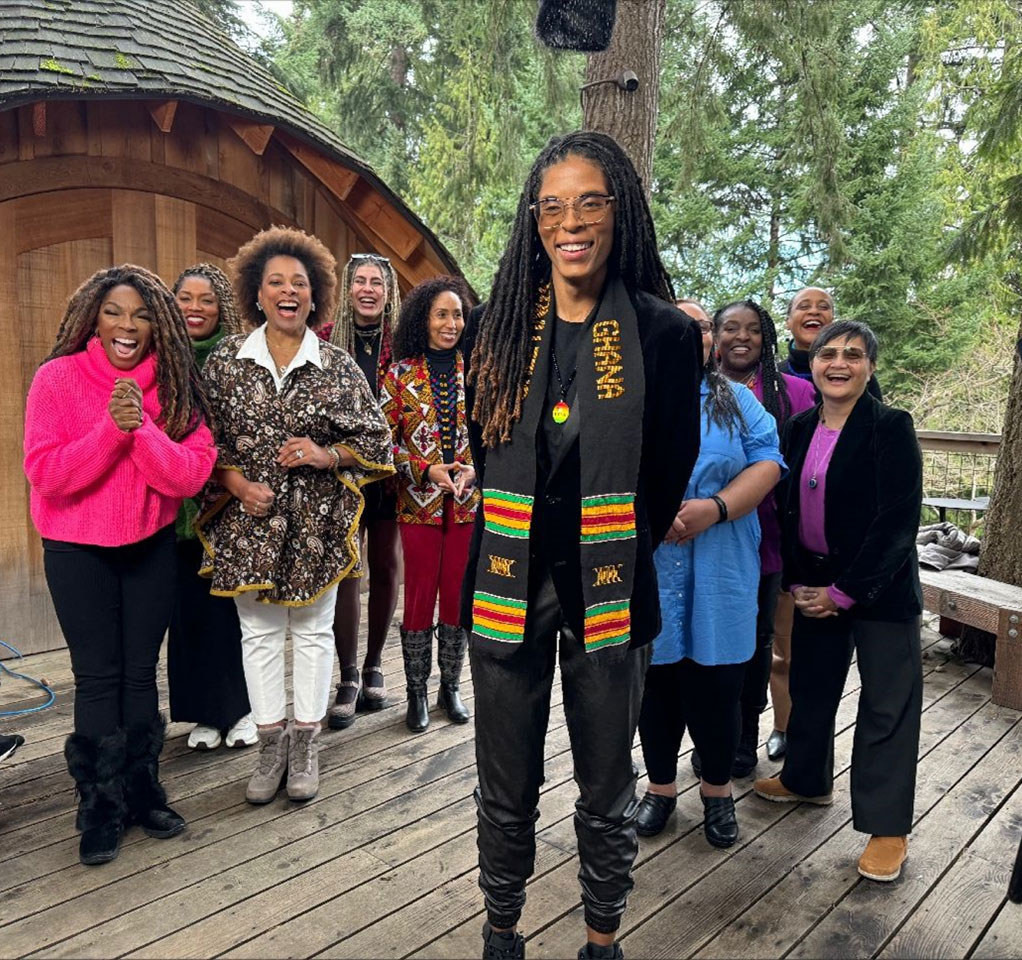 A group of people standing on a wooden deck smiling for the camera with trees in the background