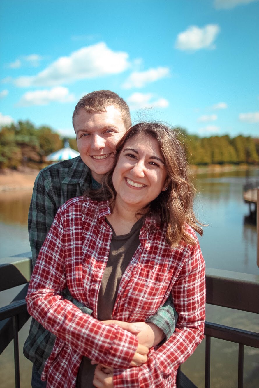 A man embracing a woman, both smiling in front of a lake behind them