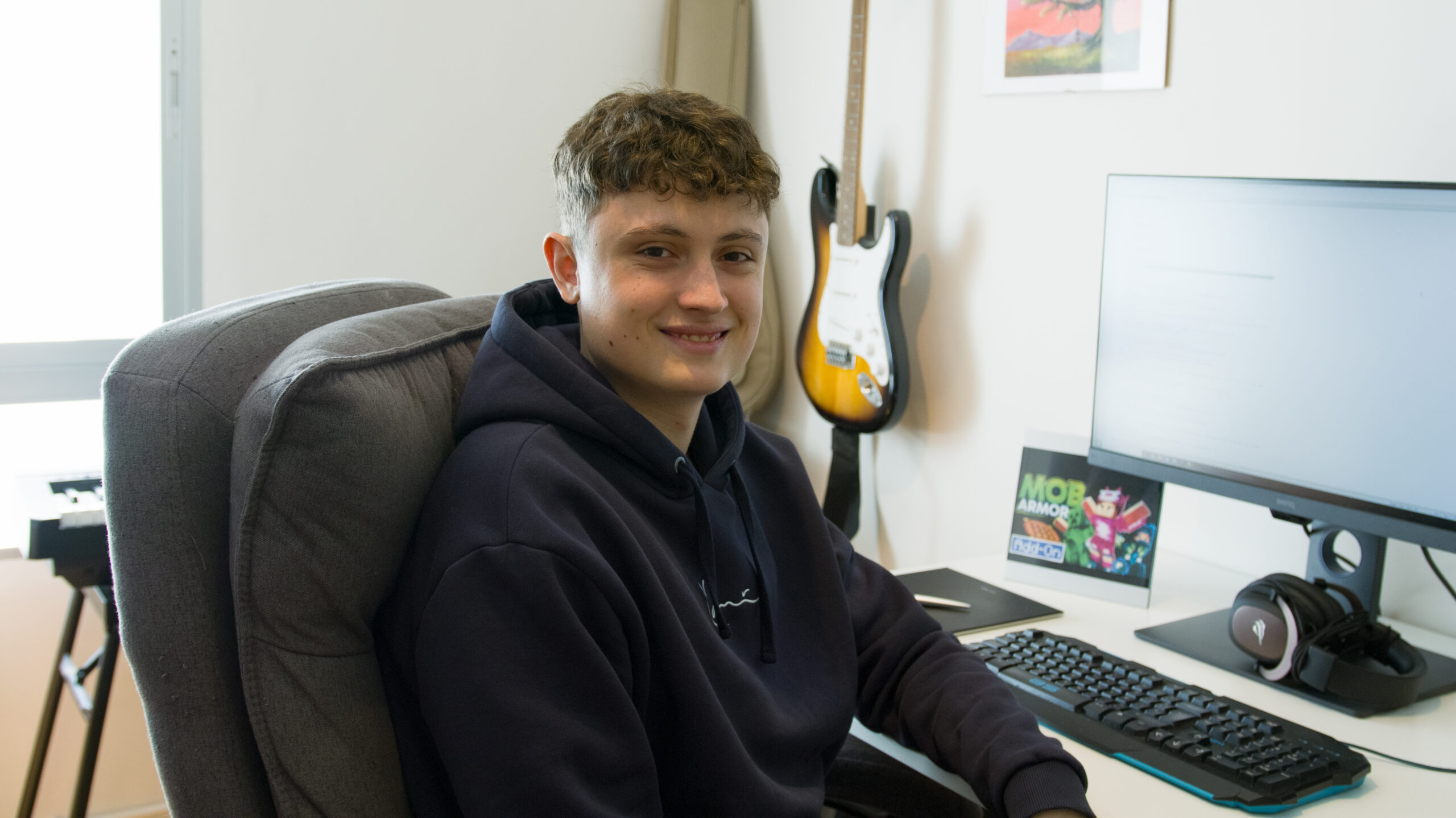 Man sitting at a desk next to a keyboard and monitor, smiling at camera