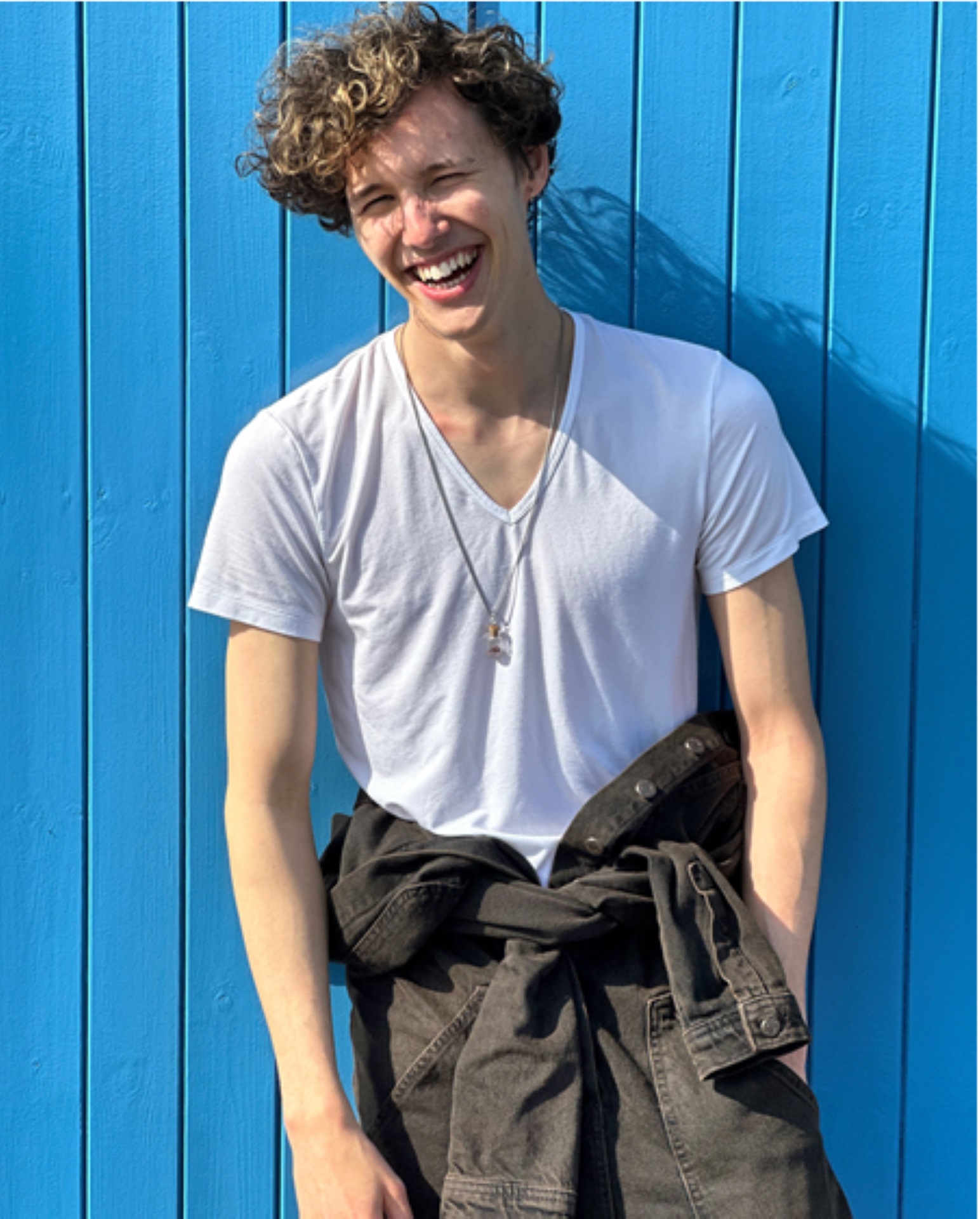 Man standing outside against a blue wall laughing