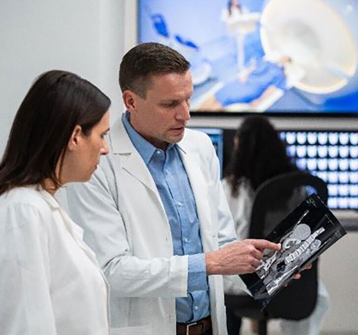Two people in medical smocks review an x-ray image on a tablet device