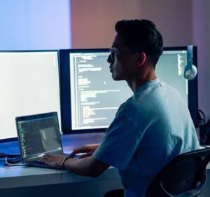 Man working at a laptop computer with two monitors
