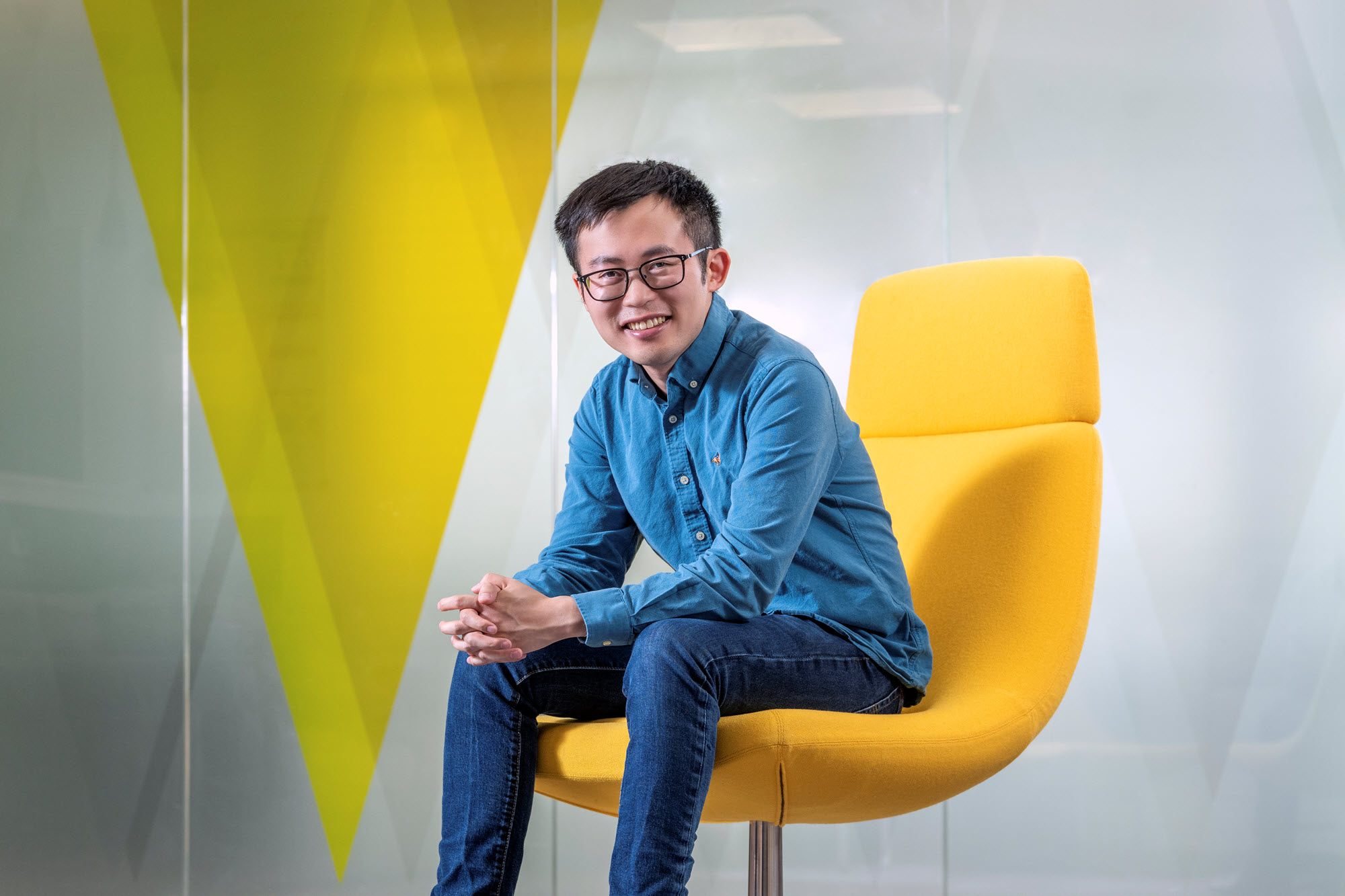 A man dressed in blue sits on a yellow chair.