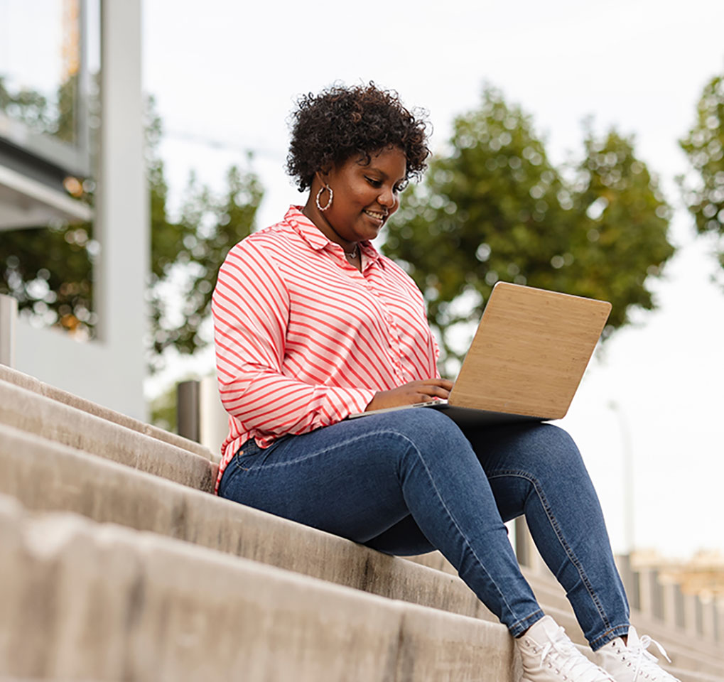 Woman sitting outside on stairs working on a laptop computer