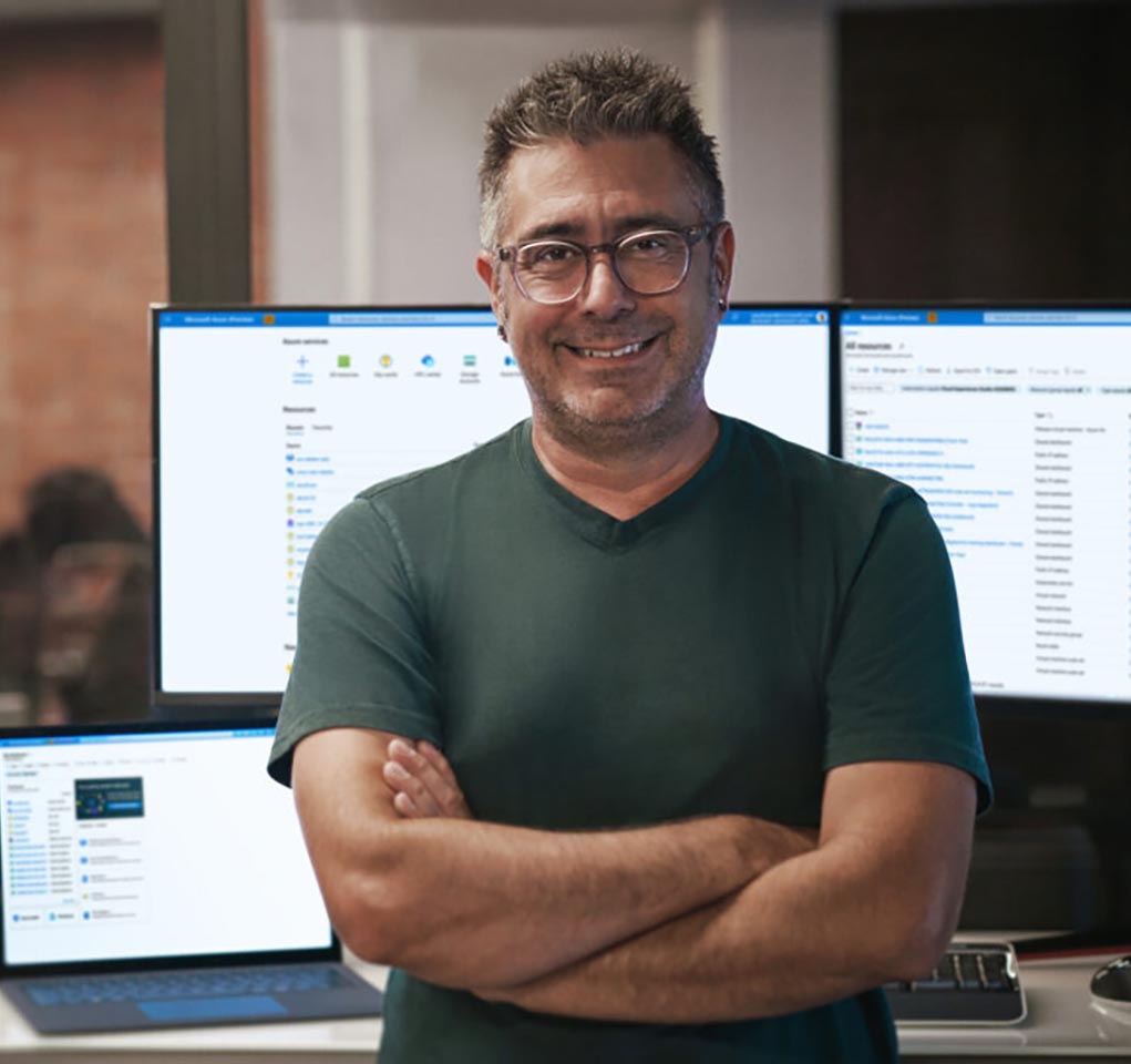 Man standing in front of computer monitors with his arms folded