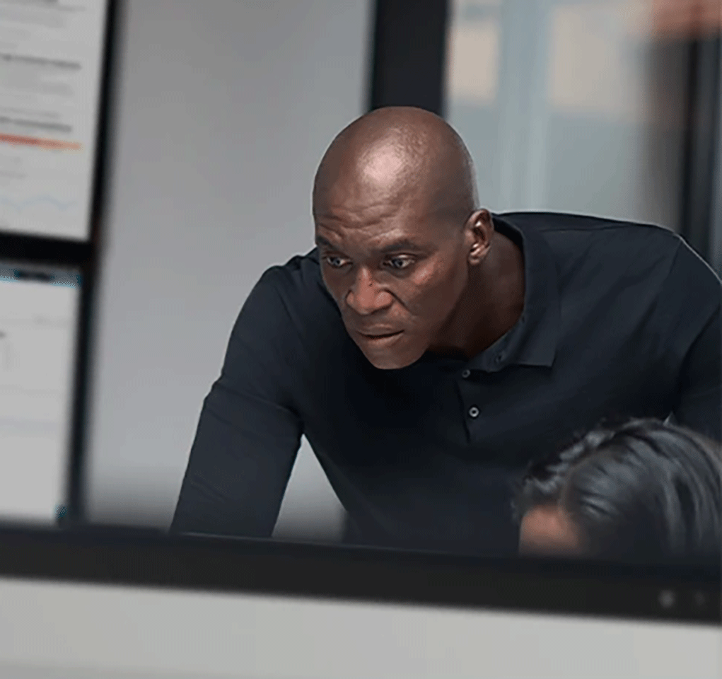 Man looks over the shoulder of someone working at a desktop monitor