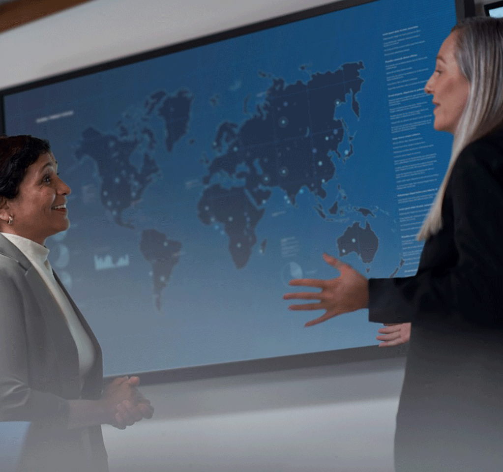 Two women talking in a conference room with a map of the world behind them