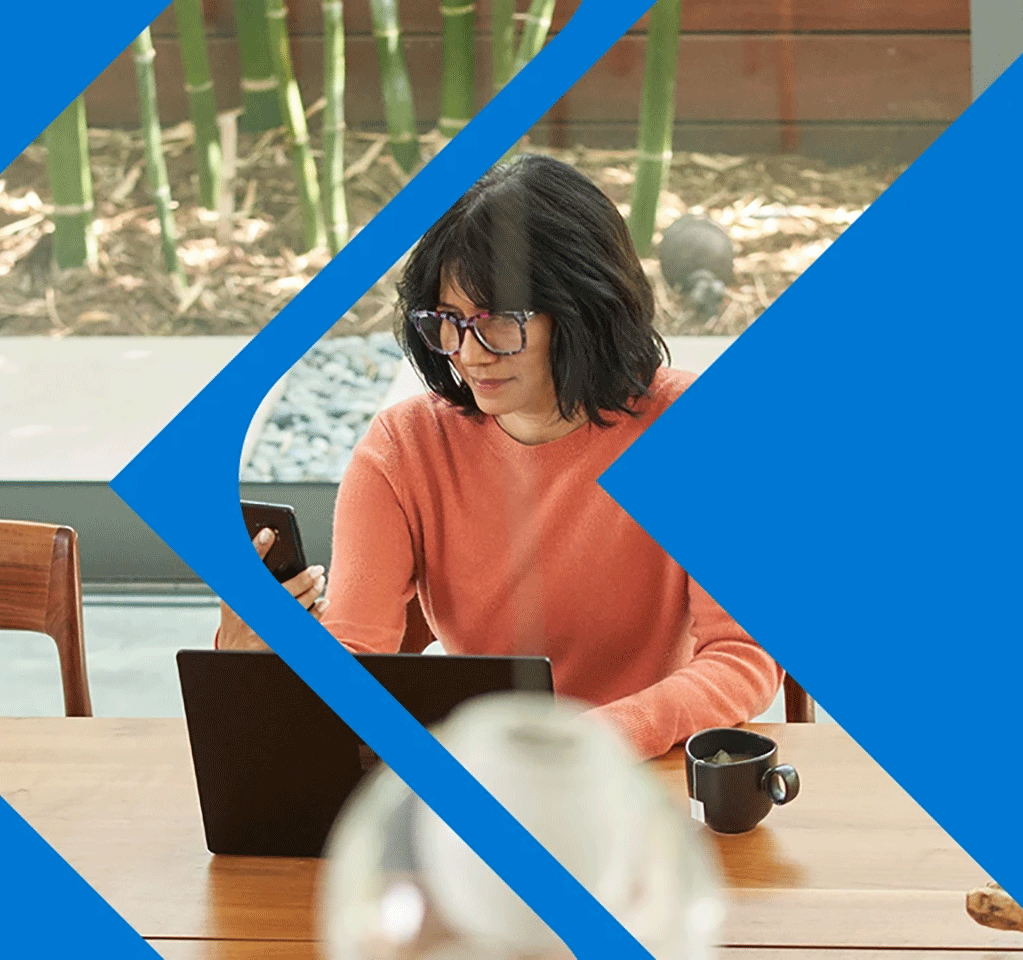 Woman looking at her phone while sitting at a laptop computer in an office