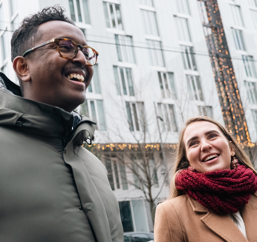 A smiling man, left, and woman wearing winter clothes on a city street.