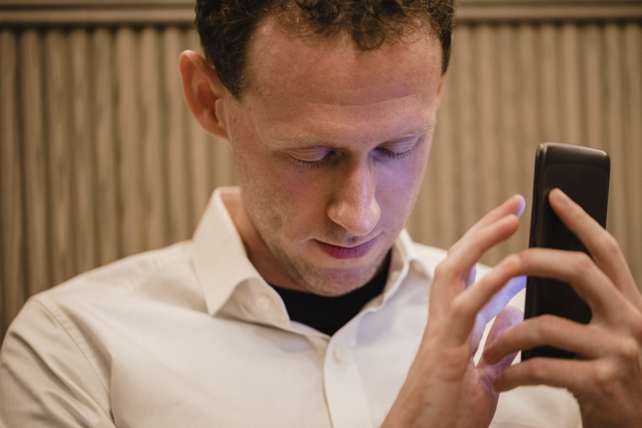 A man in a white shirt uses a smartphone.