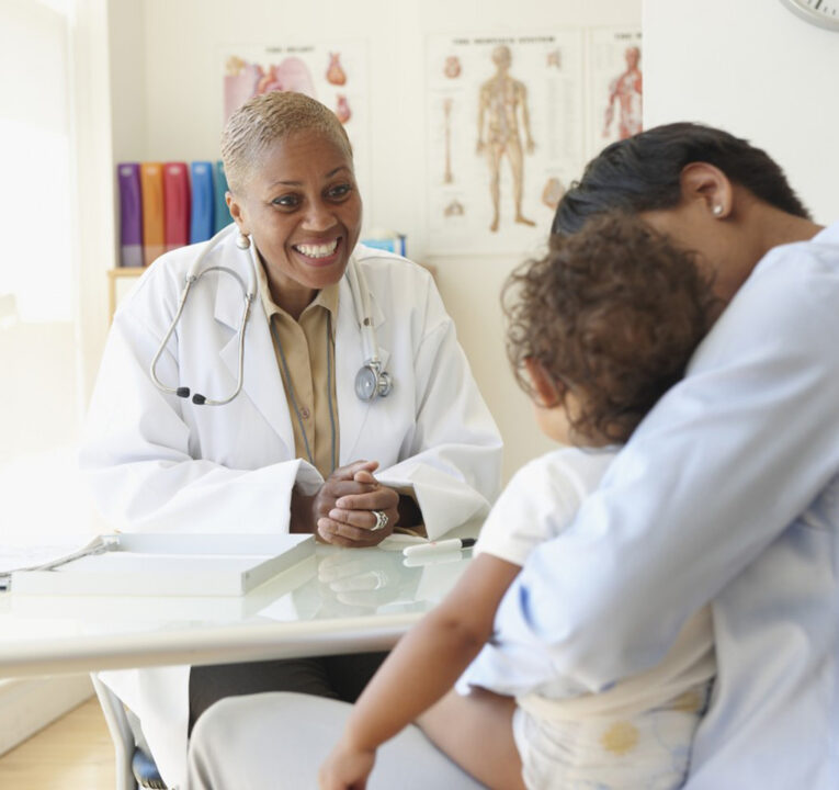 Doctor interacting with a young patient who is sitting in her mother's lap