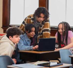 Four teenage students huddle around a laptop computer