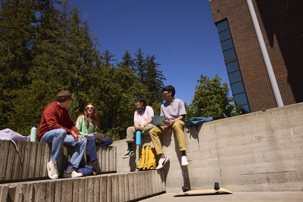 Four university students sit on a concrete structure outdoors.